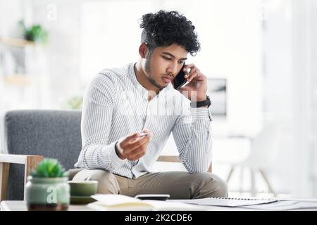 Finalising the last of is big plans. Shot of a young businessman talking on a cellphone while going through paperwork in an office. Stock Photo