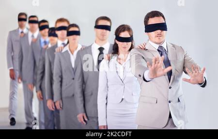 Blind leadership. A row of blindfolded businesspeople following a blindfolded leader. Stock Photo