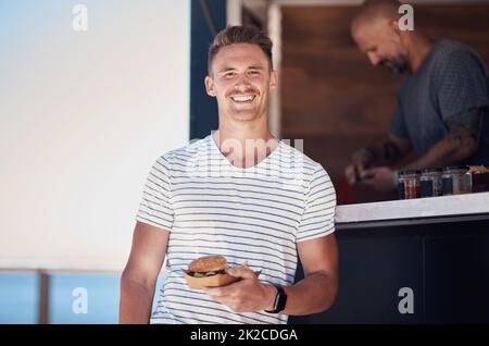 Order up. Portrait of a cheerful young waiter holding a serving of food to give to a customer outside next to a coffee truck during the day. Stock Photo