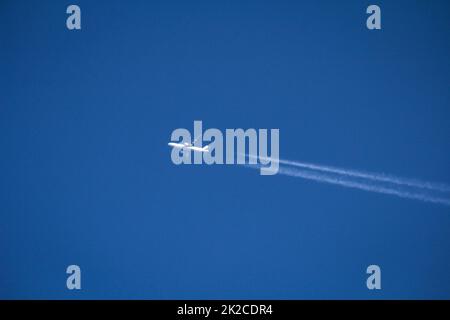 A white jet, passenger plane draws two contrails in the blue sky. Stock Photo