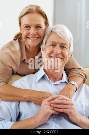 I stand behind him. Portrait of a loving senior couple holding hands in their living room. Stock Photo