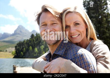 Im holding on to this one. Portrait of an affectionate mature couple sitting on a pier out on a lake. Stock Photo