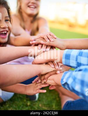 Its cool to be kind. Cropped shot of a group of kids stacking their hands on top of each other. Stock Photo