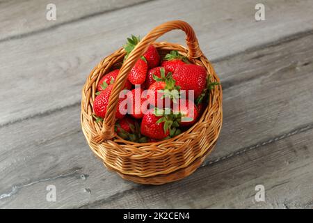 Basket full of freshly picked strawberries on gray wood desk. Stock Photo