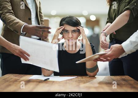 Does anyone have a headache tablet. Cropped portrait of a young businesswoman feeling overwhelmed by her colleagues in the office. Stock Photo