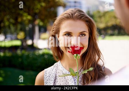 The sweet smell of love. Shot of a young woman smelling a rose her boyfriend is giving here. Stock Photo