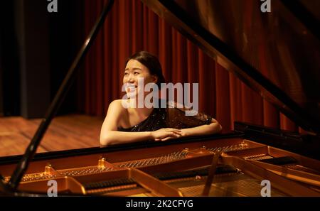 Appreciating the crowd. Shot of a young woman sitting by her piano at the end of a musical concert. Stock Photo