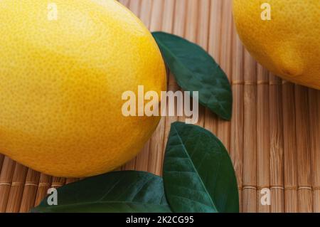 Close-up of large yellow lemons and green leaves on bamboo mat. Stock Photo