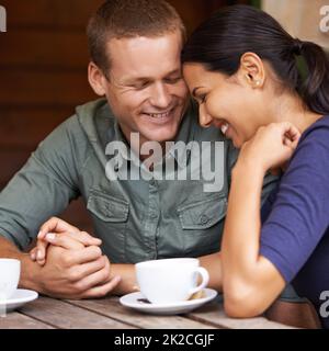 They share the same silly humour. A young multi-racial couple laughing together while drinking coffee at a cafe. Stock Photo