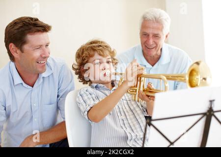 Musical talent runs in this family. Shot of a cute little boy playing the trumpet while his father and grandfather watch him proudly. Stock Photo