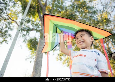 Asian happy children boy with a kite running to fly on in park Stock Photo