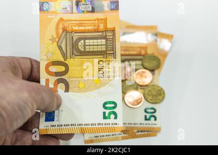 Male hand holding 50 Euro note and coins in the background Stock Photo