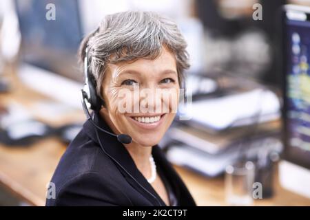 Her clients enjoy her friendly demeanor. Shot of an mature female call center representative wearing a headset. Stock Photo