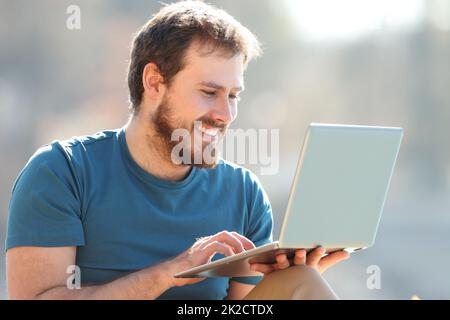 Happy man using laptop sitting in nature Stock Photo