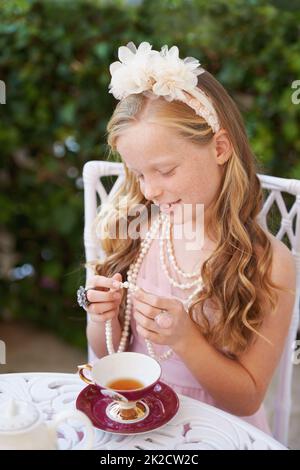 When I grow up.... A girl playing dress up in her garden with a ea cup in front of her. Stock Photo