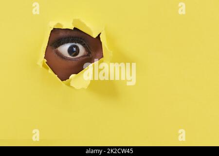 What I cant believe my eye. A view of a womanamp039s eye looking through a hole in some colorful paper. Stock Photo