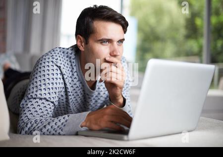 When you try to remember what your password is.... Shot of a young man contemplating while using his laptop. Stock Photo