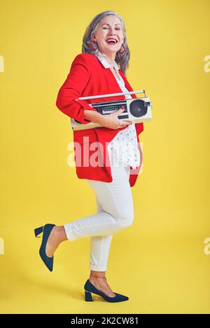 Im moving to my own rhythm today. Full length shot of a funky and stylish senior woman dancing while holding a boombox against a yellow background. Stock Photo