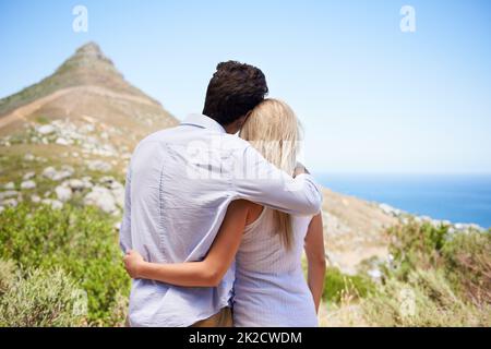 Sharing a glorious view. Rear view of a young couple embracing as they enjoy a view of the mountainside. Stock Photo