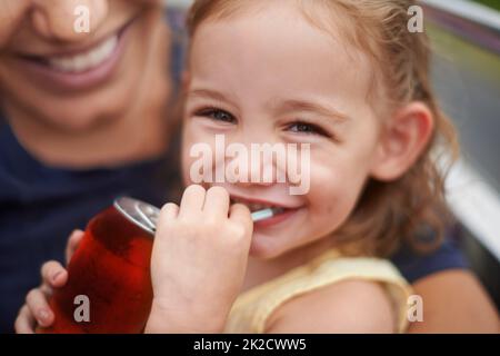 When we anywhere but home,she lets me eat and drink whatever I want. Portrait of a little girl drinking a soda on her mothers lap. Stock Photo