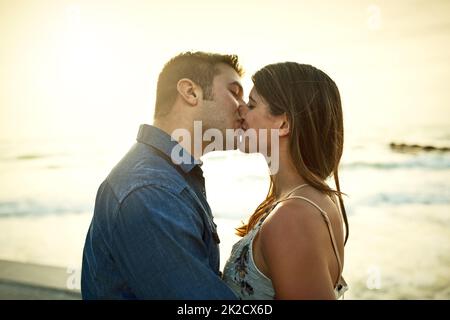 Romance in paradise. Cropped shot of an affectionate young couple kissing while standing on the beach. Stock Photo
