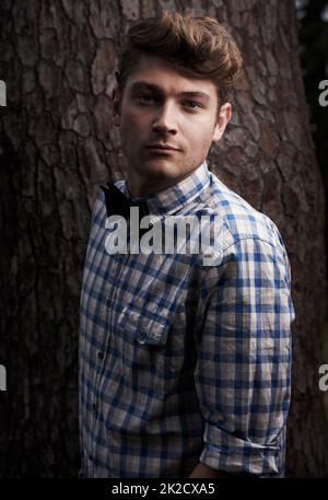 Style in the great outdoors. Portrait of handsome young hipster standing in front of a tree. Stock Photo