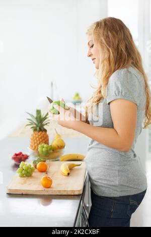 Apples are her favorite snack. Curvy and beautiful young woman cutting an apple while at her kitchen counter. Stock Photo