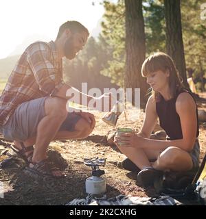 Morning coffee on the brew. Shot of a young couple making coffee on a camp stove while camping. Stock Photo