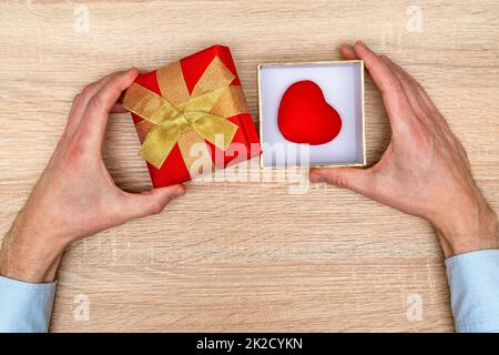 Hands opening a gift box with a tiny red heart inside Stock Photo
