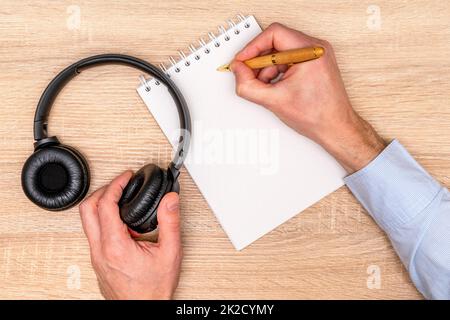 Male hands with a notebook and pen, headphones on the wooden table Stock Photo