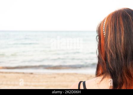 Young woman standing at the beach, looking at the sea Stock Photo