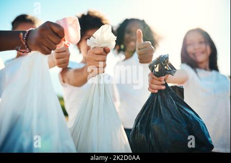 Reporting for cleanup duty. Shot of a group of teenagers picking up litter off a field and showing thumbs up at summer camp. Stock Photo