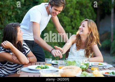 Stealing a small piece. Smiling young people at a lunch with a group of friends - portrait. Stock Photo