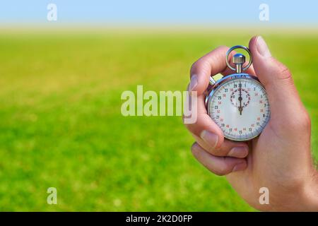 Ready for the time trials. Cropped shot of a hand holding a stopwatch against a field. Stock Photo