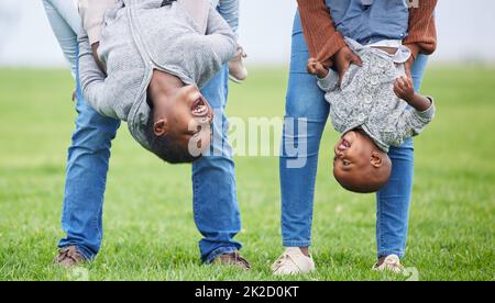 Do anything, but let it produce joy. Shot of two children hanging upside down by their parents outside. Stock Photo