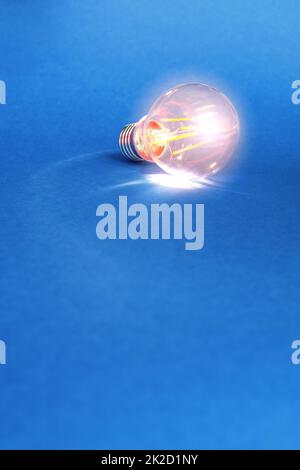 Single light bulb with light inside on blue background with copy-space. Simple minimal background for illustrating energy crisis. Stock Photo