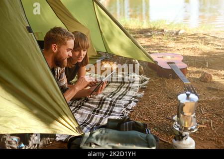 Into the woods. a young couple lying in a tent looking using a digital tablet. Stock Photo