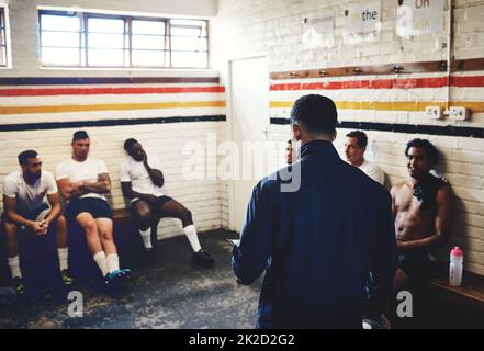 So heres what were going to do.... Cropped shot of a rugby coach addressing his team players in a locker room during the day. Stock Photo