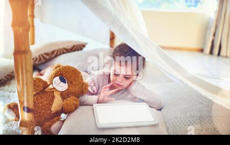 Even little kids these days know so much about technology. Shot of an adorable little girl using a digital tablet at home. Stock Photo