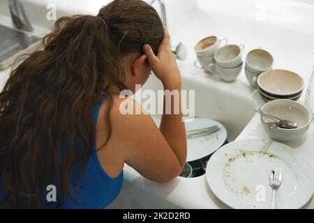 Shes had a long day. Shot of a frustrated looking woman standing by a pile of dirty dishes. Stock Photo