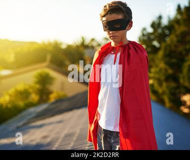Watching over his neighbourhood. Portrait of a young boy in a cape and mask playing superhero outside. Stock Photo