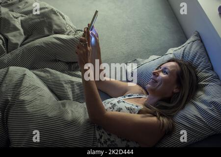 Pretty, middle-aged woman using her tablet computer before sleep in bed in the evening Stock Photo