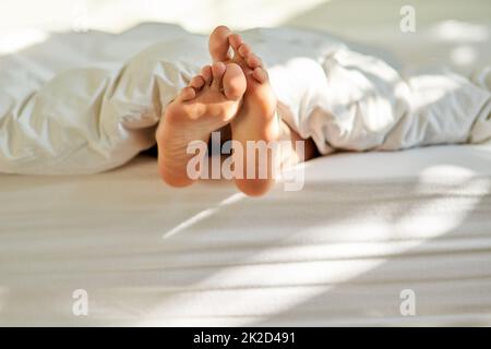 Wiggling toes of wakefulness. Shot of a mans feet poking out from the bottom of his bed. Stock Photo