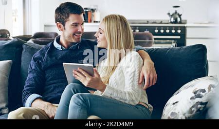 You wanna take a look. Cropped shot of an affectionate young couple using a digital tablet while sitting on their sofa at home. Stock Photo