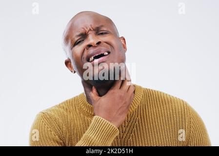 Crying out in pain. Studio shot of a young man suffering with a sore throat against a grey background. Stock Photo