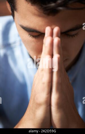 Hoping and praying. Closeup of a young man praying with his hands together. Stock Photo