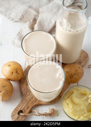 Potato milk pouring into glass on white wooden bg Stock Photo