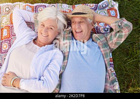 This is one relaxing retirement. Portrait of a happy senior couple relaxing together on the lawn. Stock Photo