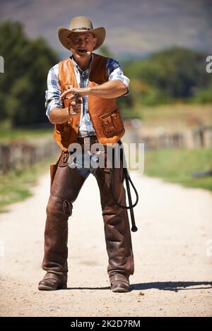 Hes the wrangler of beasts. A mature cowboy outdoors with his gun drawn. Stock Photo