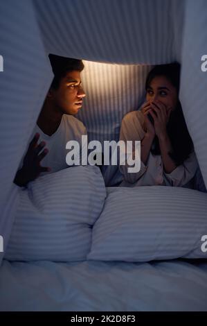 Husband telling wife scary story for under blanket Stock Photo